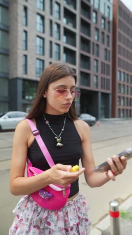 joven aplicando lápiz labial mientras usa el teléfono en la calle