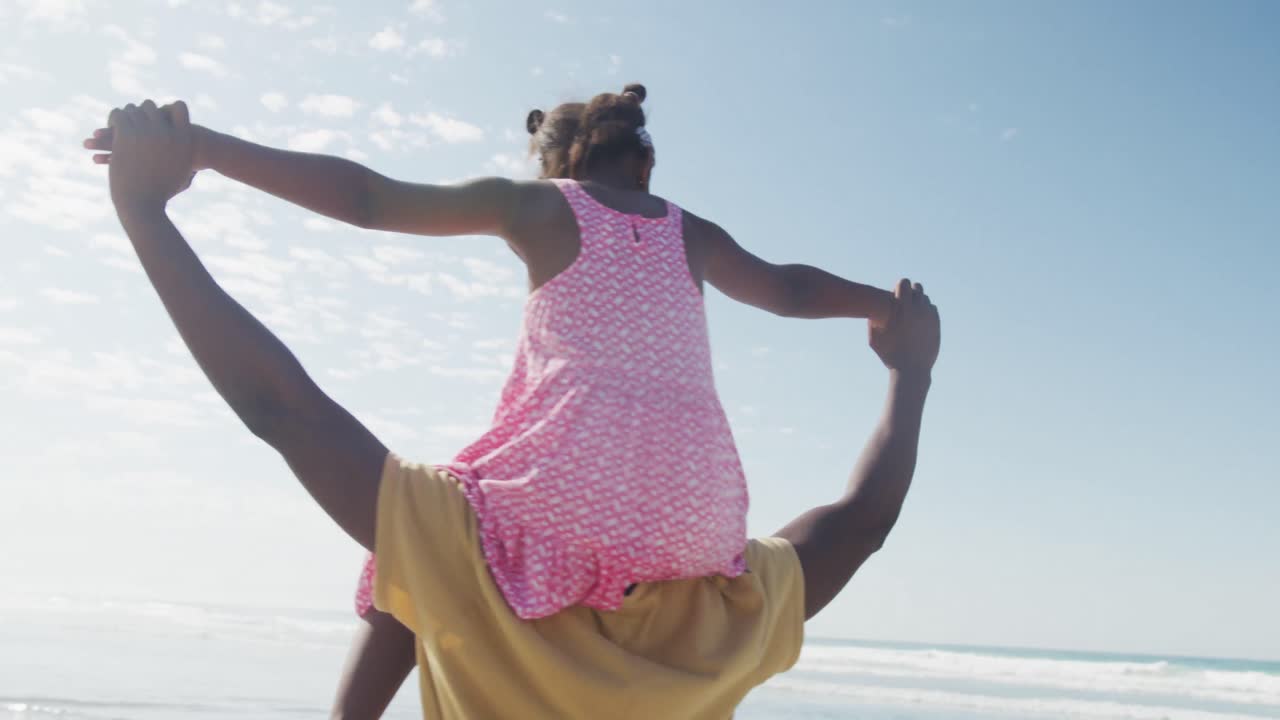 African american father carrying his daughter on his shoulders at the beach