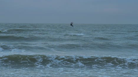 Mann-Beim-Kitesurfen,-Bewölkter-Wintertag,-Hohe-Wellen,-Ostsee-Karosta-Strand,-Zeitlupensprung,-Weit-Entfernter-Schuss