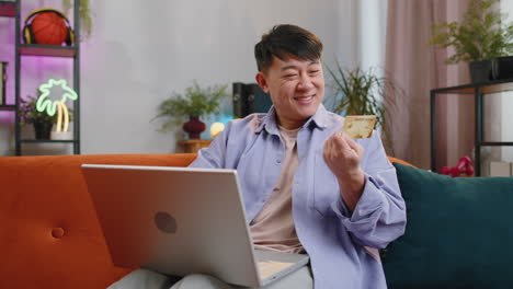 Asian adult man using credit bank card and laptop transferring money purchases online shopping