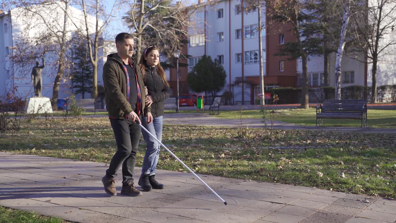 la esposa del hombre con discapacidad visual sosteniendo su brazo. están caminando en el parque.