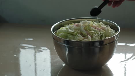 adding a spoonful of himalayan salt to stainless steel bowl of shredded cabbage for sauerkraut -static shot