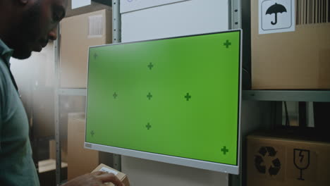 warehouse worker inspecting package near a green screen monitor