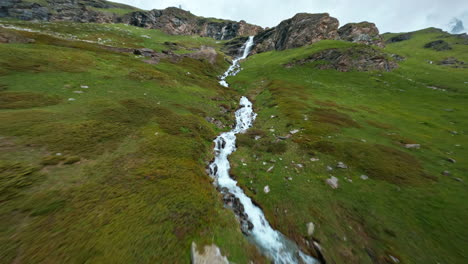 Scenic-aerial-view-of-a-mountain-stream-flowing-through-lush-green-meadows-near-Cervinia