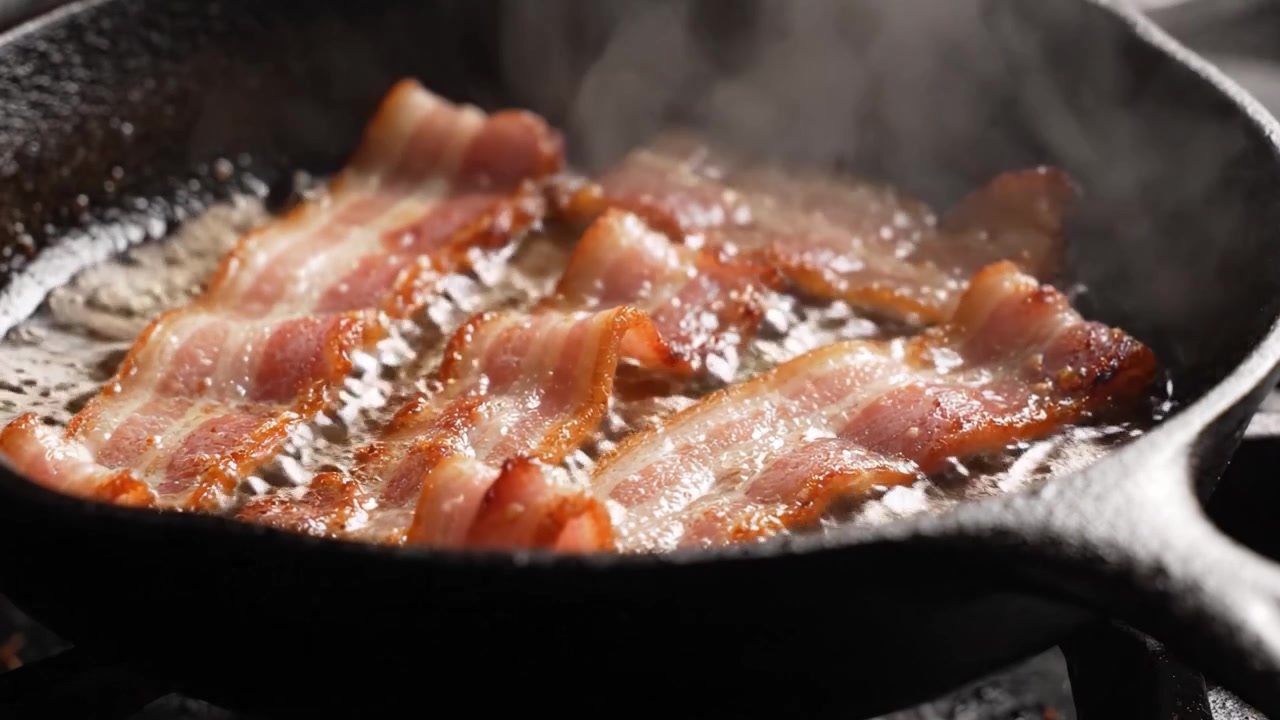 Bacon sfrigolante in una padella di ghisa: strisce fritte alla perfezione con bordi croccanti e un delizioso aroma che riempie la cucina.