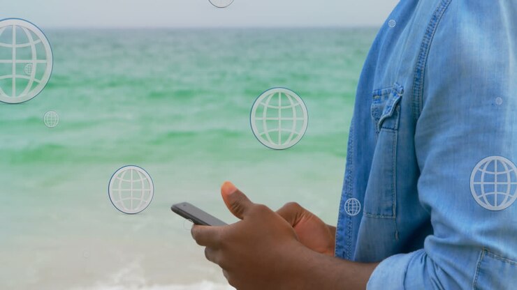 Animation of globes over midsection of african american man using smartphone at beach