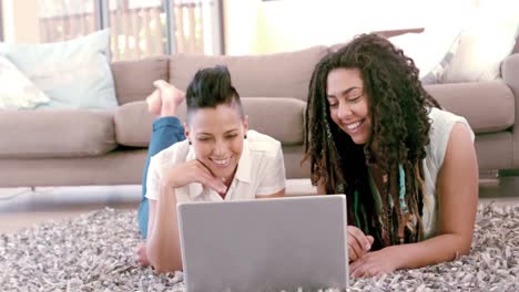 una feliz pareja de lesbianas usando una computadora portátil en la alfombra
