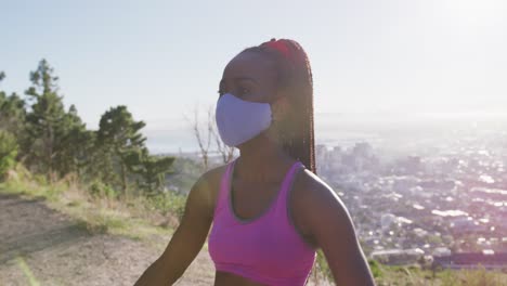 mujer afroamericana con máscara facial estirando los brazos al aire libre