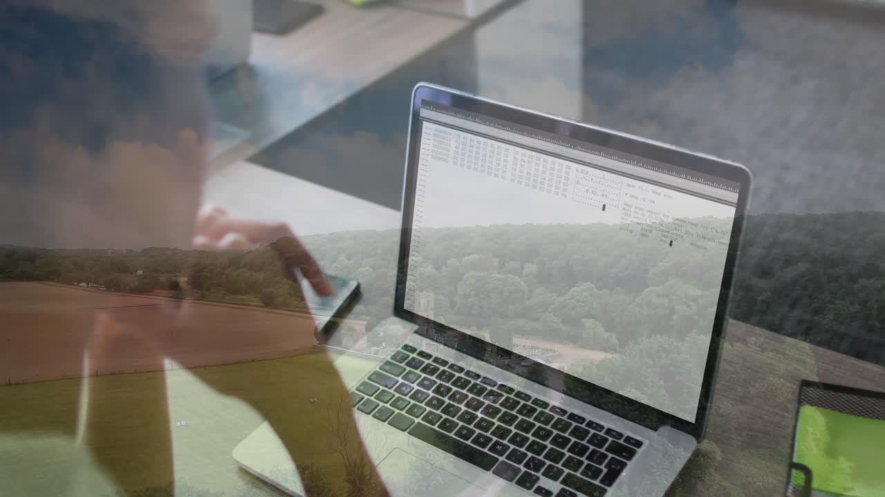 Using laptop with code overlay, person working with animation on scenic landscape