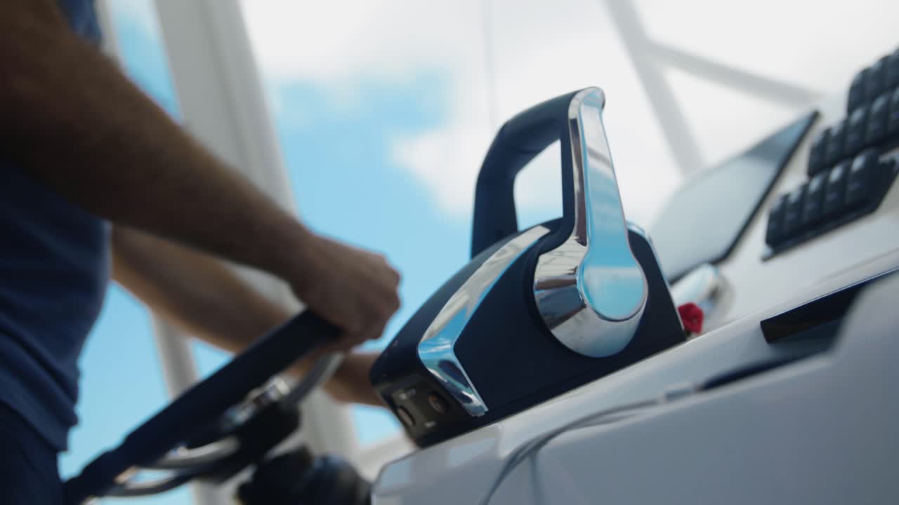 A man navigates a luxury boat, hands on the helm and speed control lever, the wind gently blowing