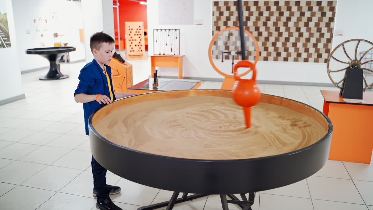 a little boy visiting a science museum for children. He plays with a sand pendulum