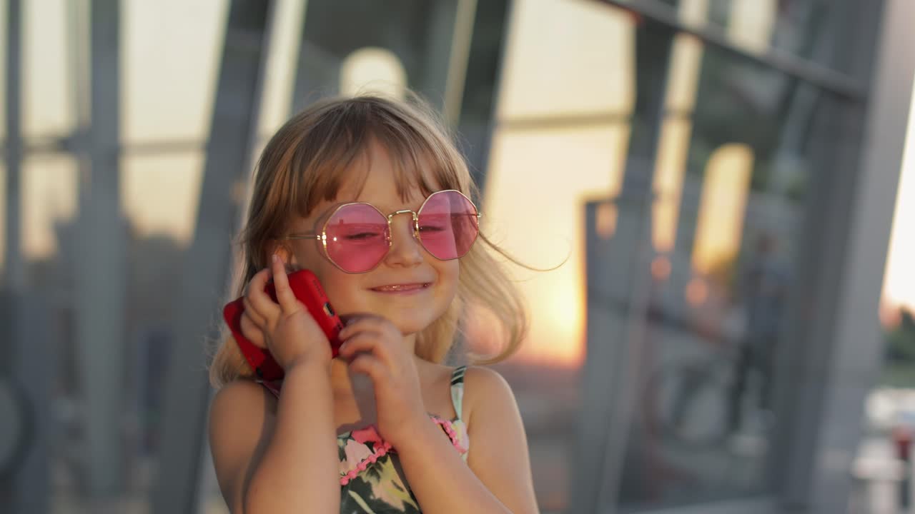 Menina turista usando óculos de sol estilosos usa o telefone. Criança usando smartphone para ligar, conversar. Turismo.