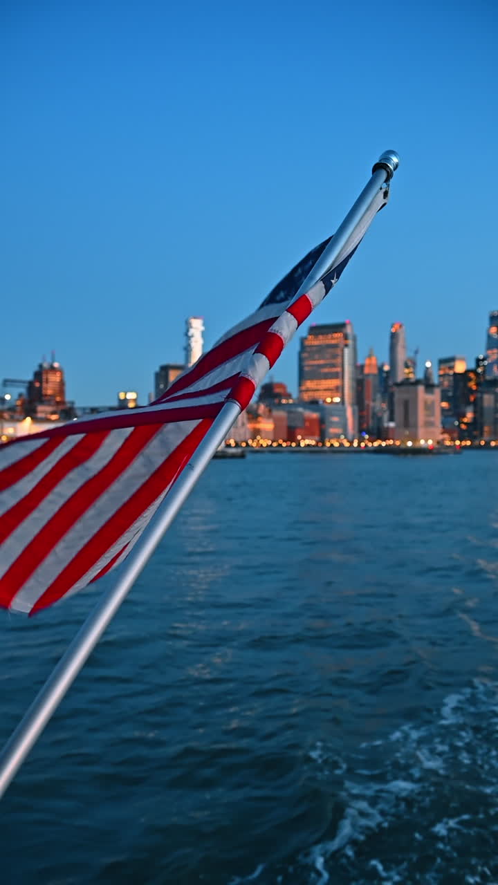 Bandiera americana che sventola con lo skyline di New York sullo sfondo. Primo piano di una bandiera americana che sventola su una barca con lo skyline di New York sfocato sullo sfondo al crepuscolo