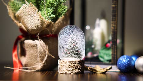 Christmas-Tree-Snow-Globe-Decoration-On-The-Table-With-Glittery-Baubles-On-The-Side
