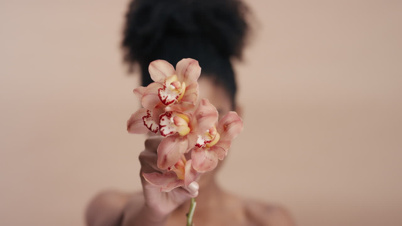 ritratto di bellezza bella donna afroamericana che posa giocosamente con un fiore di orchidea toccando una pelle sana che gode di una dolce fragranza di essenza naturale concetto di cura della pelle