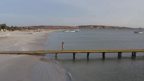 brunette latina in swimsuit walking on the pier in coche island, venezuela by drone