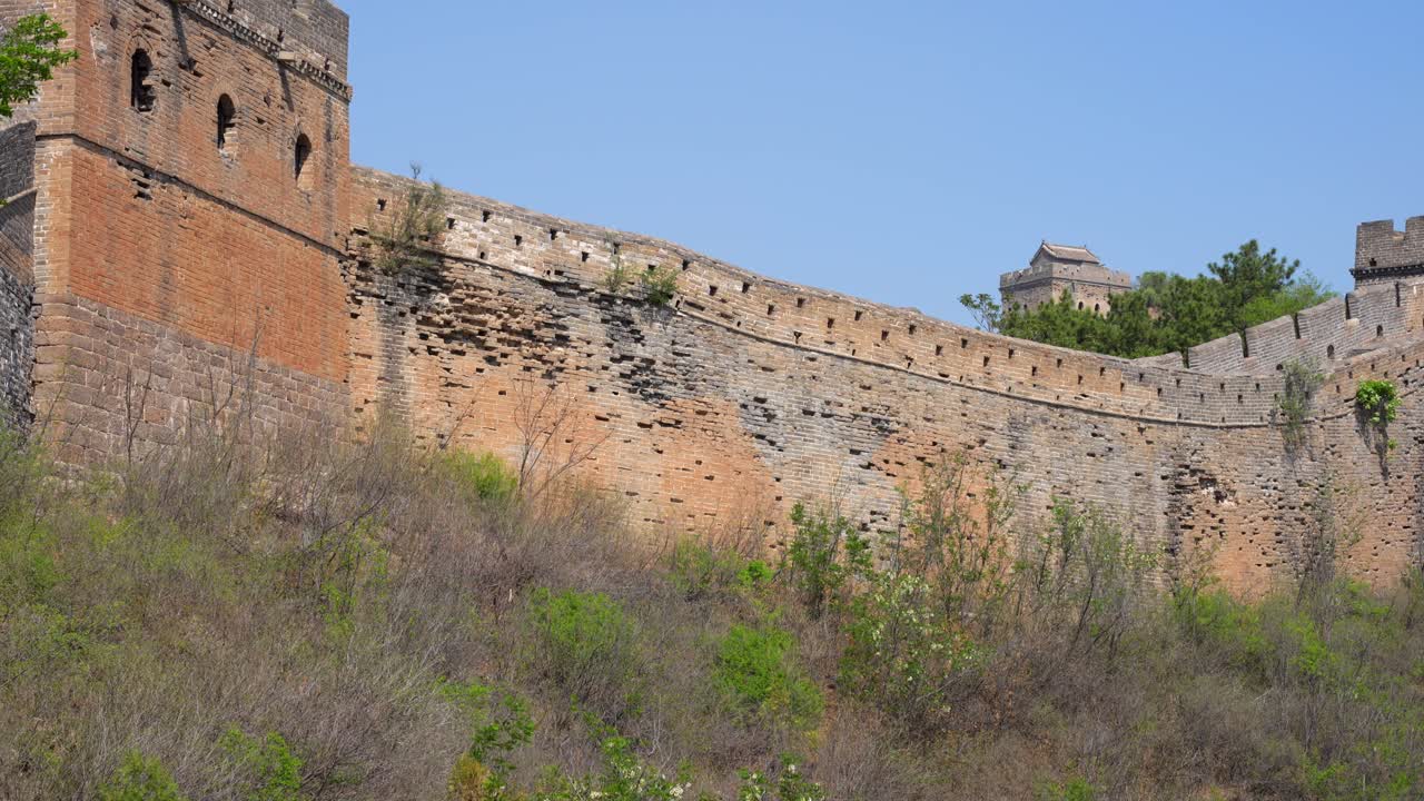 Deteriorated Great Wall section with a rugged watchtower and greenery in Beijing