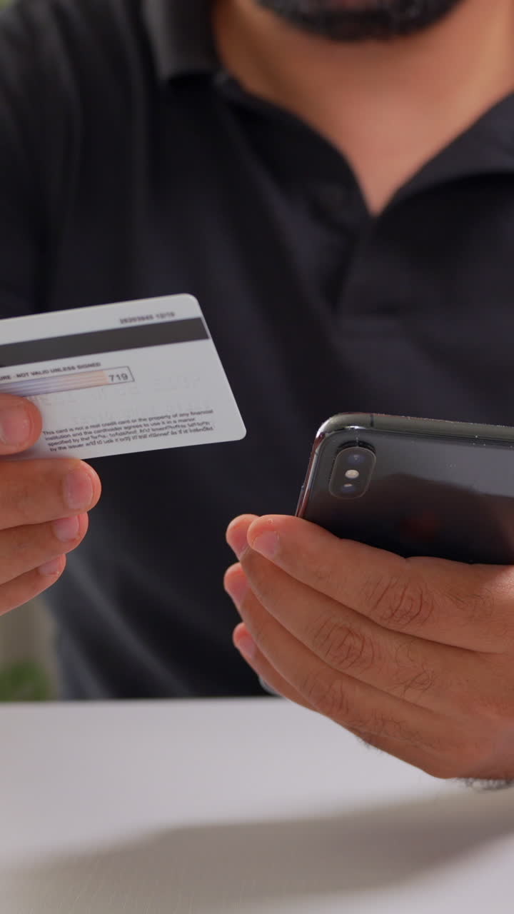 Close-up of a person holding a smartphone and credit card, engaging in online shopping. Soft lighting enhances the focused, modern atmosphere in this vertical video