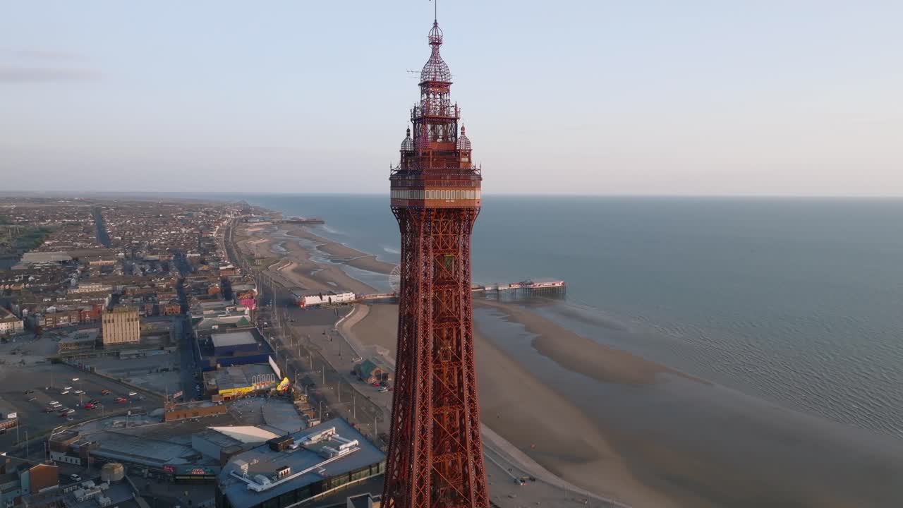 Blackpool promenade and Blackpool Tower with piers at golden hour. Slow orbit. Lancashire, UK.
