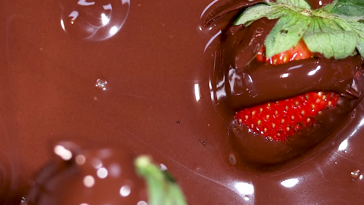 A vibrant strawberry partially submerged in smooth, melted chocolate, highlighting its glossy texture and rich color.