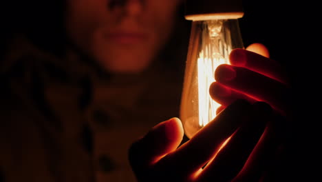 sad man warms his hands near a light bulb in the dark