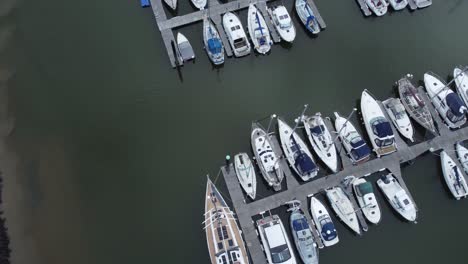 top down aerial drone view above luxury moored private marina sailing ships and yacht boats orbit tilt up left shot