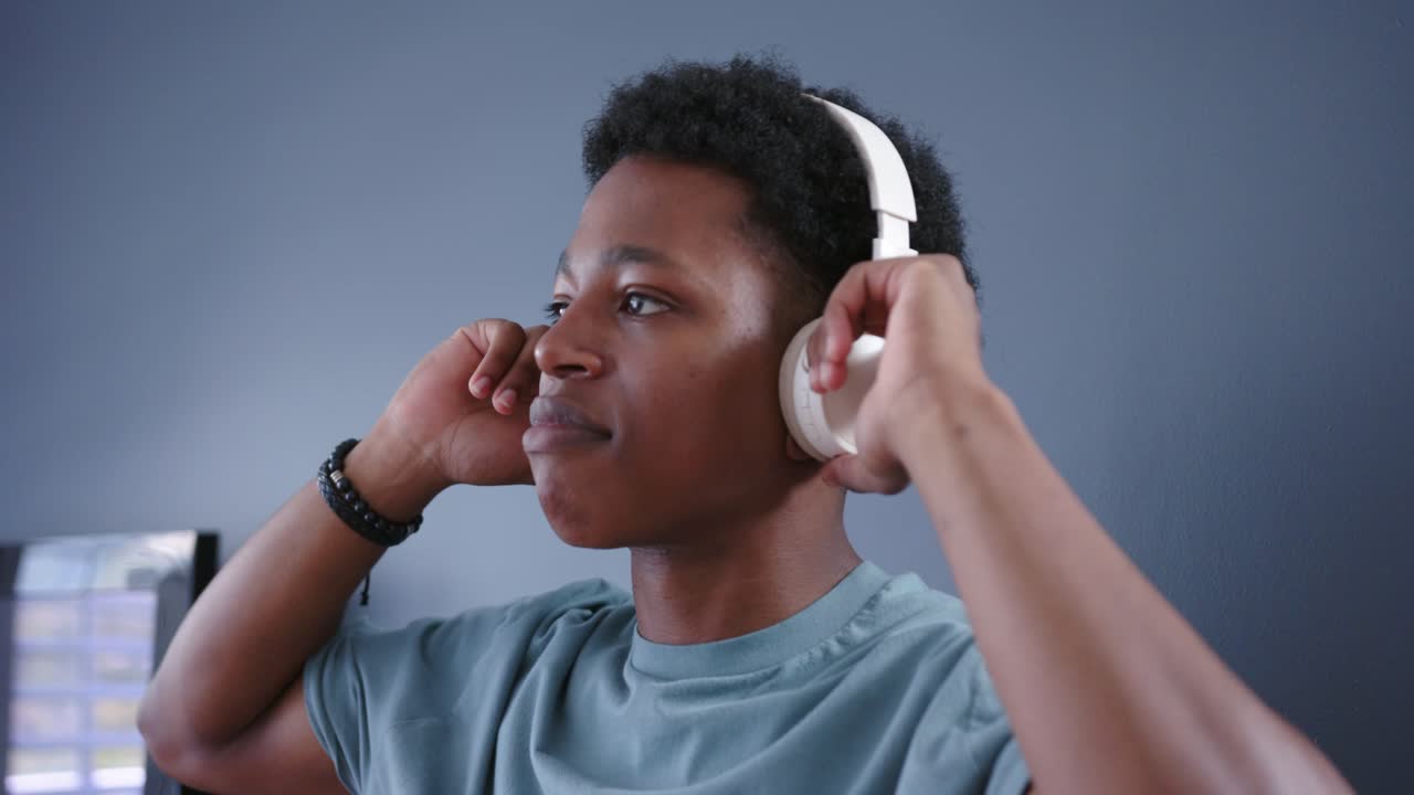 Uomo che, in una stanza, solleva le mani per indossare cuffie over-ear bianche, regolando i padiglioni e testando vestibilità e audio.