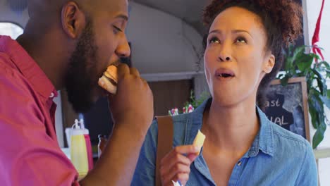 primer plano de una pareja afroamericana comiendo hamburguesas y papas fritas juntos en el camión de comida