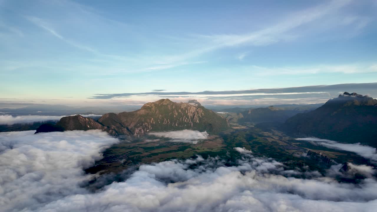 Aerial view of mountain peaks emerging from clouds during sunrise in Vang Vieng