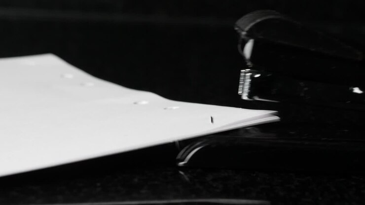 Primo piano di una cucitrice che pinza fogli di carta, isolata su sfondo nero
