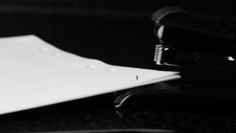 close up of stapler, stapling sheets of paper isolated on black background