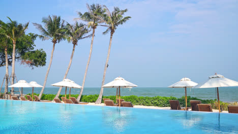 umbrella-with-bed-pool-around-swimming-pool-with-ocean-sea-background---holiday-and-vacation-concept