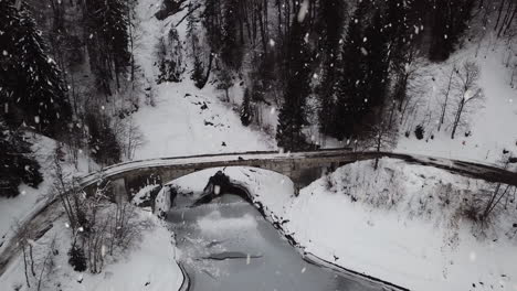 puente de piedra cubierto de nieve durante las nevadas en el majestuoso paisaje de colinas, vista aérea de descenso