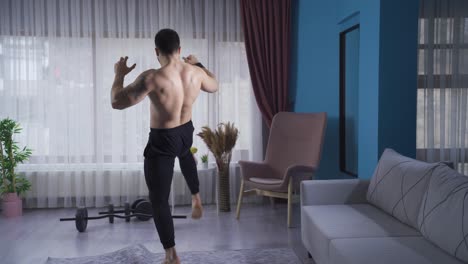 young athlete doing kickboxing against the air at home with his back turned.