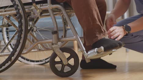 close up of male nurse's hands helping a patient in wheelchair putting feet on footrest and pushing him to another room after a physical therapy at home