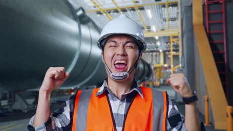 close up of asian male engineer with safety helmet standing and screaming goal celebrating working in pipe manufacturing factory