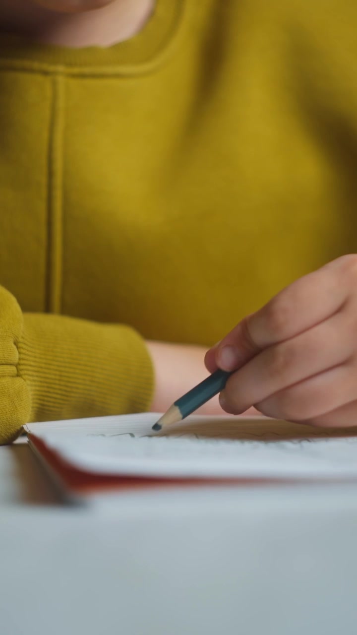 Primo piano di un bambino concentrato che disegna su un quaderno mentre indossa le cuffie