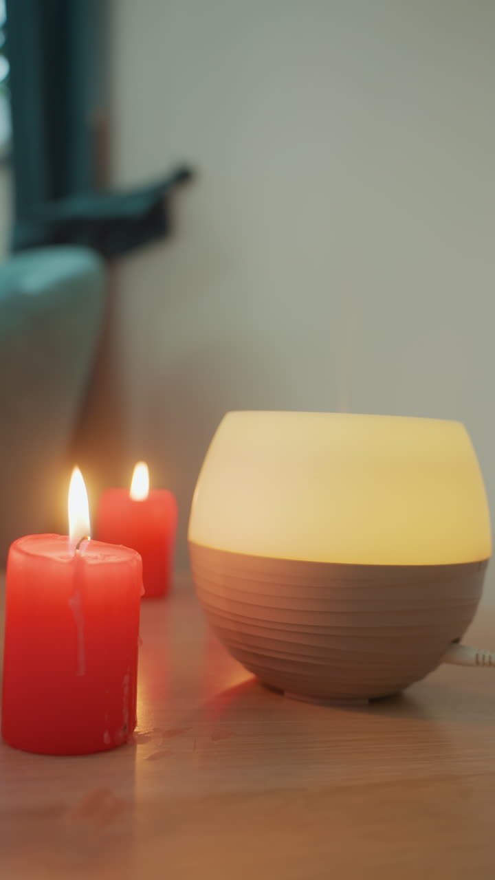 Scène de spa chaleureuse éclairée aux bougies avec micro-courants lumineux sur une table en bois à côté de bougies rouges, une main s'apprête à régler l'appareil, lueur douce et chaude, rituel de soin du soir serein, ambiance apaisante idéale.