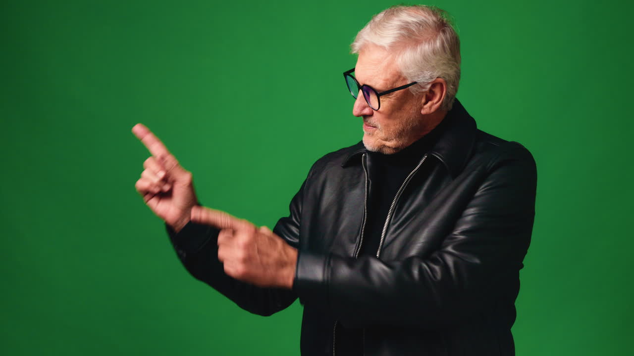 Senior man in leather jacket pointing on green screen