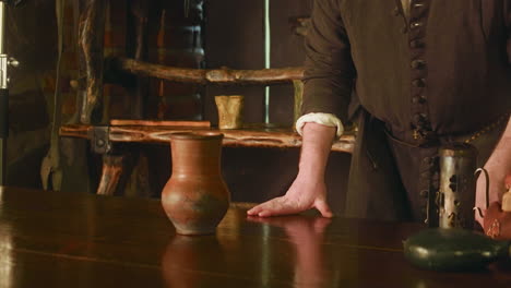 bartender leans on counter in medieval tavern. attentive barkeeper in brown dress listens to guest order in store. visiting ancient bar adventure