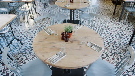 elevated view of empty tables and chairs in a restaurant with tiled floor and feature window and stone wall, handheld