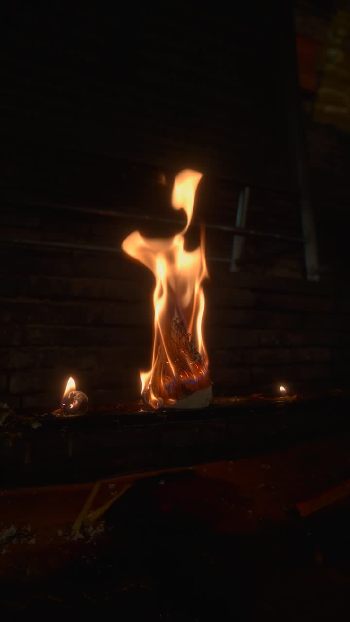 Flames rise from burning Buddhist offering at night temple ritual, glowing spiritual ceremony, vertical