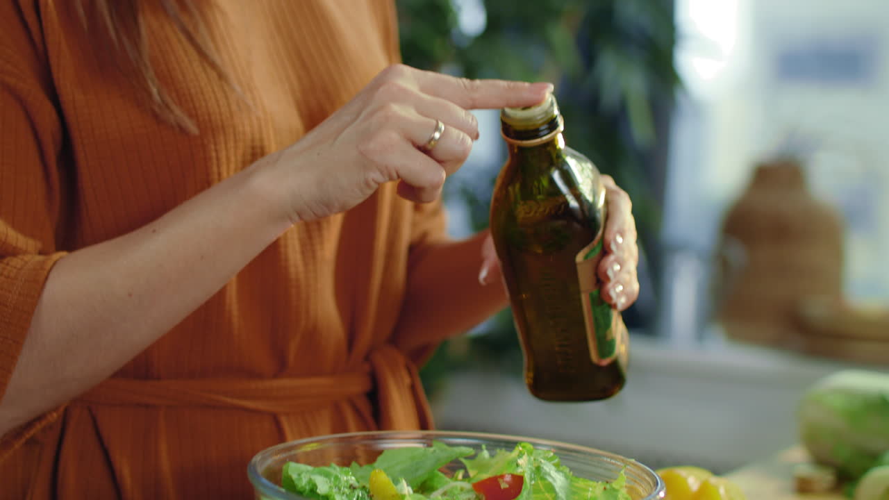 Woman hands pouring olive oil in mixing bowl. Brunette making vegetable salad.