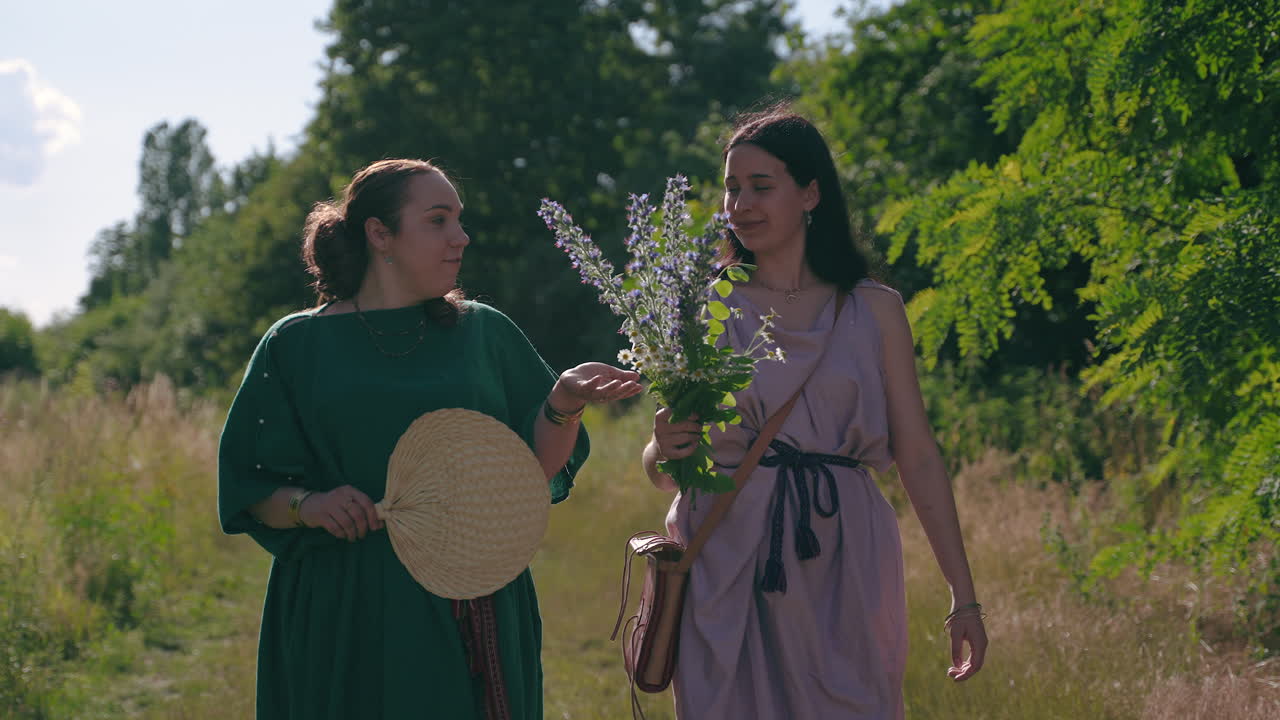Two Women in Historical Costumes Walking Through a Meadow