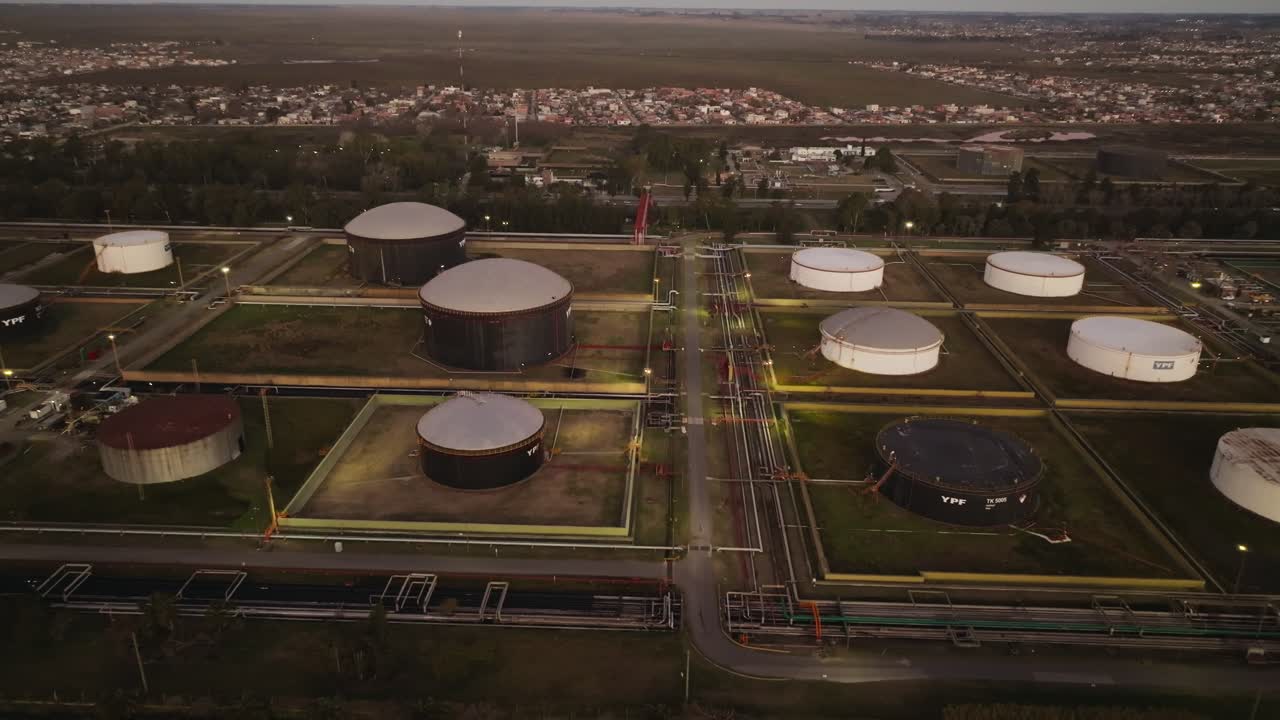 Aerial drone shot moving toward large open-air oil storage tanks, capturing the scale and layout of the oil plant