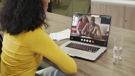biracial woman using laptop for video call, with diverse business colleagues on screen