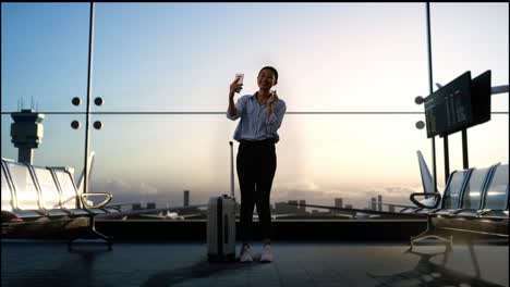 cuerpo lleno de mujer asiática con maleta rodante en la sala de embarque en el aeropuerto, haciendo selfie por teléfono inteligente mientras espera el vuelo, el avión despegue fuera de la ventana