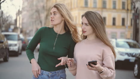 Two-Tourist-Friends-In-The-City-Search-For-An-Address-On-The-Cell-Phone