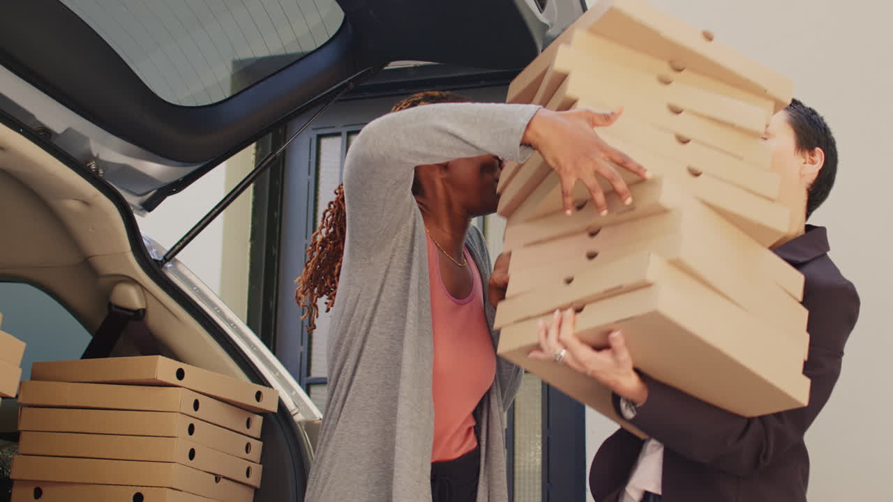 Two women taking pizza boxes out of car