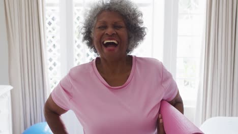 Portrait-of-senior-african-american-woman-holding-yoga-mat-smiling-at-home